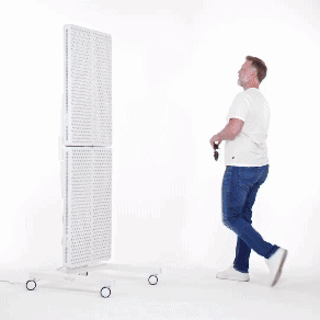 Mężczyzna w białej koszulce i niebieskich dżinsach obraca duży, pionowy, perforowany panel LED na kółkach, obracając go poziomo na białym tle.