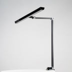 Lampa biurkowa heilys charakteryzuje się nowoczesnym, minimalistycznym designem z regulacją natężenia światła, smukłą prostokątną głowicą, regulowanym metalowym ramieniem i podstawą zaciskową - idealne oświetlenie biurowe, pokazane na prostym białym tle.