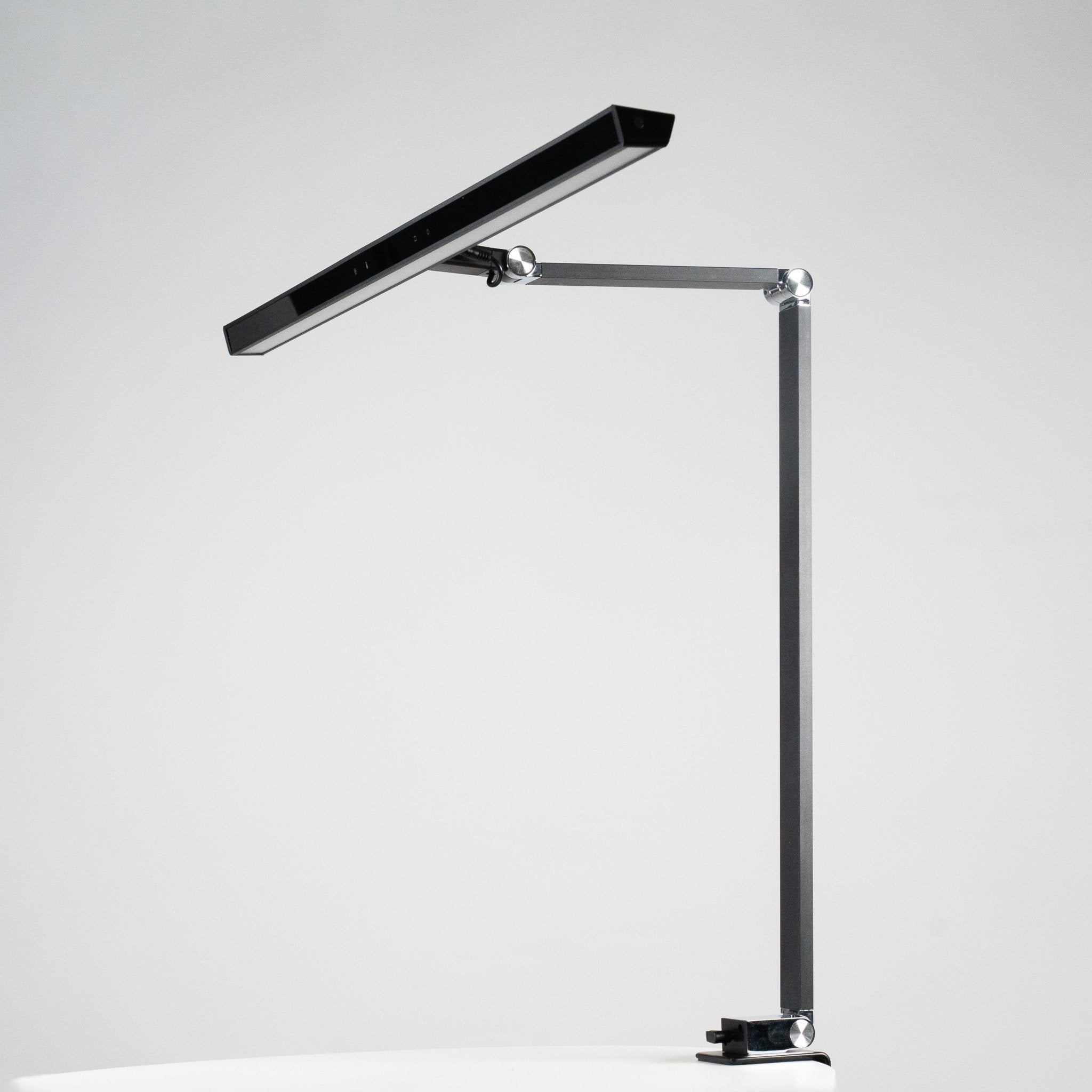 Lampa biurkowa heilys charakteryzuje się nowoczesnym, minimalistycznym designem z regulacją natężenia światła, smukłą prostokątną głowicą, regulowanym metalowym ramieniem i podstawą zaciskową - idealne oświetlenie biurowe, pokazane na prostym białym tle.