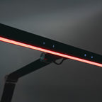 Zbliżenie na lampę biurkową heilys LED z regulacją natężenia, świecącym czerwonym paskiem świetlnym, dotykowym sterowaniem i eleganckim czarnym minimalistycznym designem idealnym do oświetlenia biurowego na neutralnym tle.