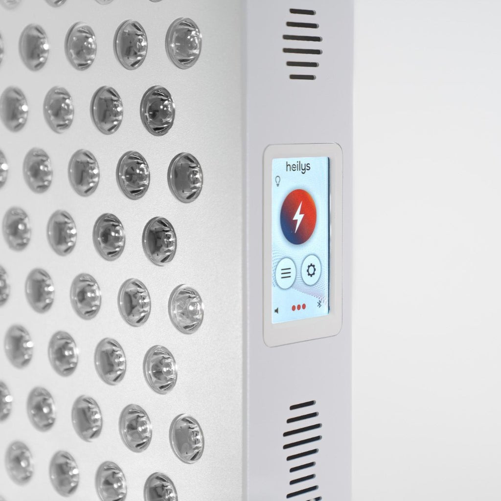 Zbliżenie białego panelu LED Heilys przedstawia rzędy okrągłych świateł i ekran dotykowy z czerwoną ikoną błyskawicy i nazwą marki, podkreślając jego zastosowanie w terapii światłem.
